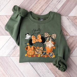 May include: Green sweatshirt with a Halloween-themed graphic. The design includes a Minnie Mouse bow, pumpkin, ghost, spiderwebs, and the text "Literally just a girl." The graphic also features a coffee drink and heart-shaped sunglasses.
