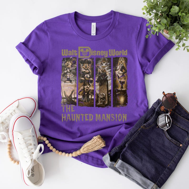 May include: Purple t-shirt featuring a graphic of Mickey Mouse and other characters from the Haunted Mansion ride at Walt Disney World. The text "Walt Disney World" and "The Haunted Mansion" is printed on the shirt.