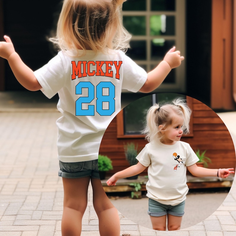 May include: Two children wearing white t-shirts. The child in the back is wearing a white t-shirt with the text "MICKEY 28" in orange and blue. The child in the front is wearing a white t-shirt with a cartoon image of Mickey Mouse playing basketball.