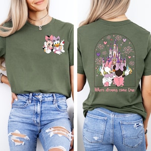 Pu&ograve; includere: Una maglietta verde con un'immagine di cartone animato di Minnie Mouse e Daisy Duck sul davanti. La parte posteriore della maglietta ha un'immagine di cartone animato di Minnie Mouse e Daisy Duck di fronte a un castello rosa con il testo "Where dreams come true".
