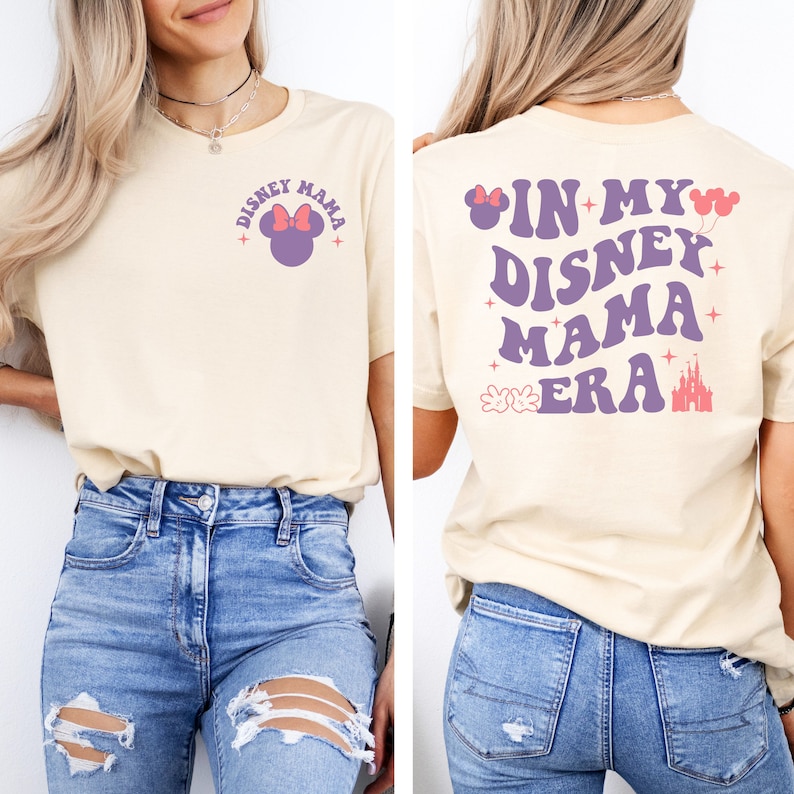 May include: A light beige t-shirt with the text "Disney Mama" and a purple Mickey Mouse head with a pink bow on the front. The back of the shirt has the text "In My Disney Mama Era" in purple with pink accents.