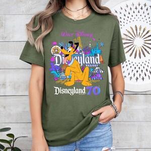 May include: A green t-shirt with a colorful graphic of Pluto and Disneyland text. The text reads "Walt Disney Disneyland Resort Disneyland 70".