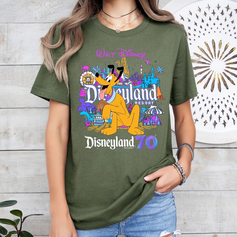 May include: A green t-shirt with a colorful graphic of Pluto and Disneyland text. The text reads "Walt Disney Disneyland Resort Disneyland 70".