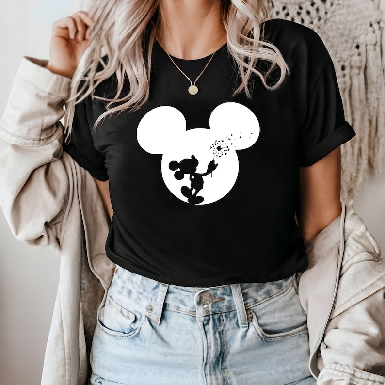 May include: Black t-shirt with a white silhouette of Mickey Mouse blowing on a dandelion.