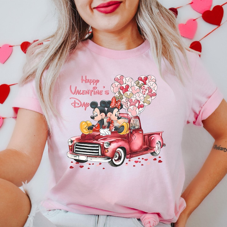 May include: Pink t-shirt with a graphic of Mickey and Minnie Mouse in a red pickup truck with a heart-shaped balloon bouquet that says "Happy Valentine's Day".
