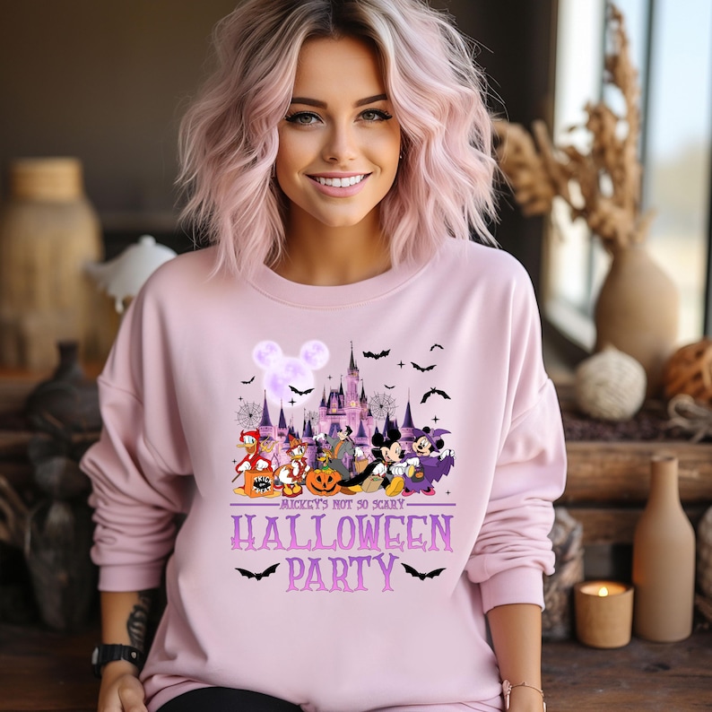 Puede incluir: Sudadera rosa con un gr&aacute;fico morado y blanco de Mickey Mouse y sus amigos frente al castillo de Disney. El texto "Mickey's not so scary Halloween Party" est&aacute; impreso en la sudadera.