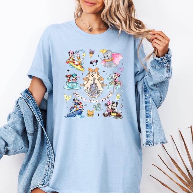May include: Light blue t-shirt with a colorful illustration of Mickey Mouse and friends at Disney World. The text "Best Day Ever" is printed on the shirt.