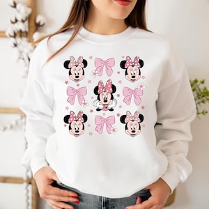 May include: White sweatshirt with a pink and red Minnie Mouse print. The print features Minnie Mouse's face with a pink bow and polka dots. The print is repeated multiple times on the sweatshirt.