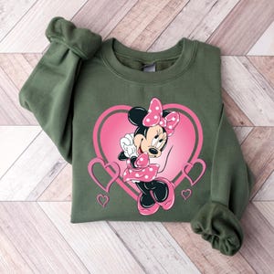 May include: Green sweatshirt with a pink heart design featuring Minnie Mouse in a pink and white polka dot dress.