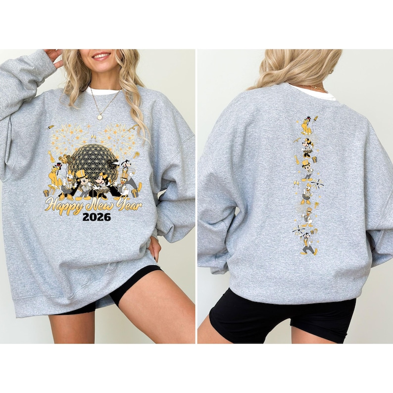 May include: A light gray sweatshirt with a graphic design featuring a large sphere, fireworks, and cartoon characters. The text "Happy New Year 2026" is printed below the graphic. The back of the sweatshirt has a vertical line of cartoon characters.
