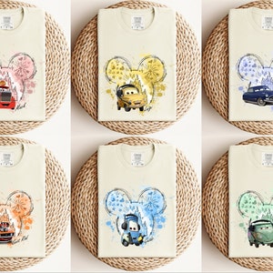 Puede incluir: Seis camisetas diferentes con un dise&ntilde;o de cabeza de Mickey Mouse que presenta un coche de la pel&iacute;cula Cars de Disney Pixar. Cada camiseta tiene un fondo de color diferente y un coche diferente. Las camisetas est&aacute;n todas sobre una superficie de mimbre marr&oacute;n claro.