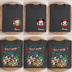 Op de afbeelding: Donkergrijze t-shirts met kerstthema Disney-personageontwerpen. E&eacute;n shirt toont Donald Duck met "Becca", een ander Mickey Mouse met "Daddy", en een derde met "Mommy". De andere shirts hebben een Disney World 1971 ontwerp.