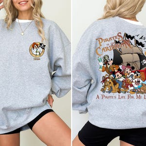 May include: Gray sweatshirt with a cartoon image of characters from the Pirates of the Caribbean ride. The text "Pirates of the Caribbean" and "A Pirate's Life For Me Lyrics" are printed on the sweatshirt.