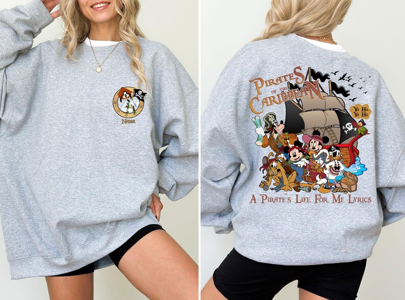May include: Gray sweatshirt with a cartoon image of characters from the Pirates of the Caribbean ride. The text "Pirates of the Caribbean" and "A Pirate's Life For Me Lyrics" are printed on the sweatshirt.