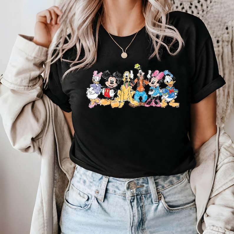 Puede incluir: Camiseta negra con un estampado gr&aacute;fico colorido de Mickey Mouse y sus amigos. Los personajes est&aacute;n dispuestos en l&iacute;nea, con Mickey Mouse en el centro.