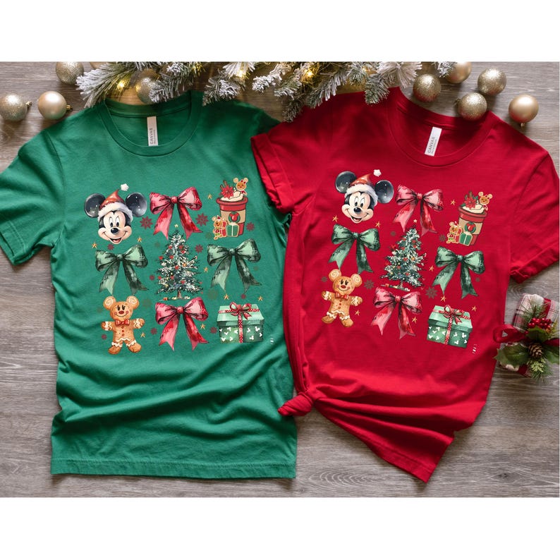 May include: Two Christmas themed t-shirts, one green and one red, featuring a Mickey Mouse design with bows, a gingerbread man, a Christmas tree, and presents.
