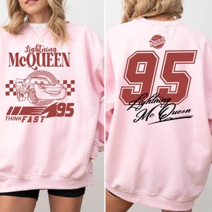May include: Pink sweatshirt with a red graphic of Lightning McQueen from the Cars movie. The graphic includes the text "Lightning McQueen", "Think Fast", and "95".