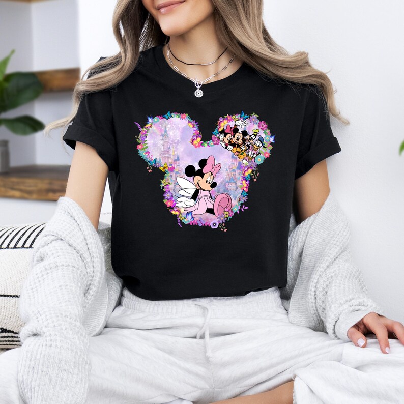 May include: Black t-shirt with a floral design featuring Mickey Mouse ears. The design includes a pink Minnie Mouse with a bow and a pink dress. The design also includes a castle and other Disney characters.