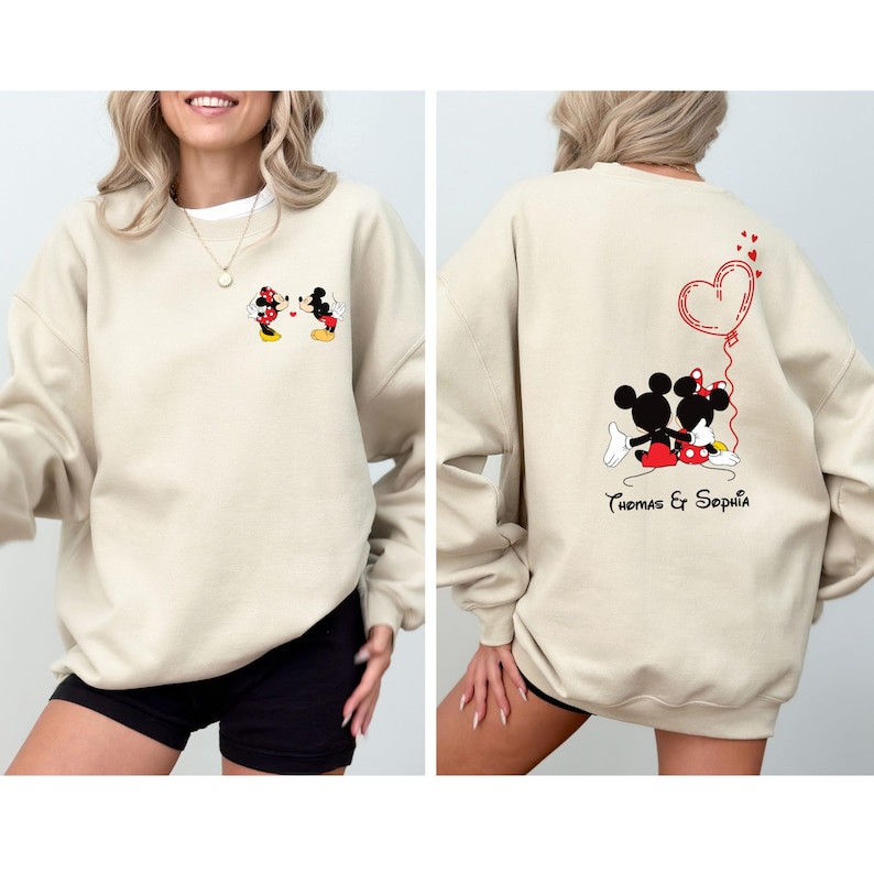 May include: A beige sweatshirt with a Mickey Mouse and Minnie Mouse graphic on the front and a Mickey Mouse and Minnie Mouse graphic with a red heart balloon and the text "Thomas & Sophia" on the back.