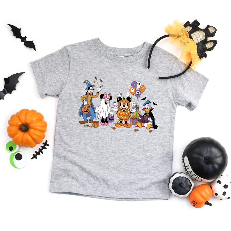 May include: A gray t-shirt featuring a Halloween-themed graphic of Disney characters, including Mickey Mouse, Goofy, and Donald Duck, dressed in costumes. The image includes pumpkins, bats, and a headband.