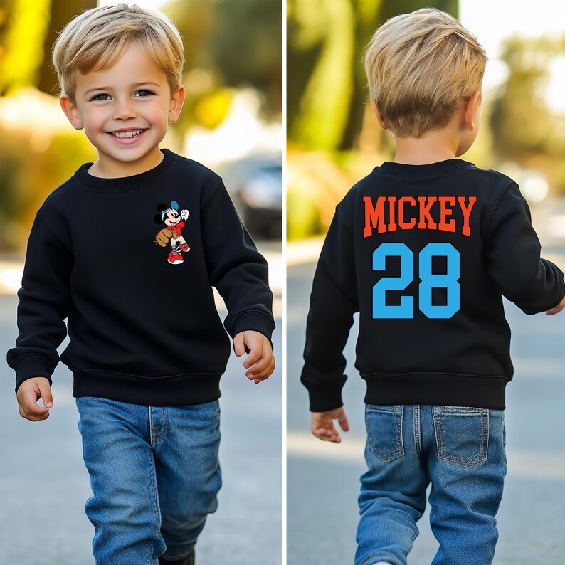 May include: Black sweatshirt with a Mickey Mouse graphic on the front and "MICKEY 28" text on the back. The child is wearing blue jeans.