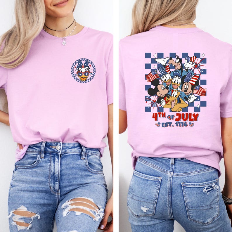 Puede incluir: Camiseta rosa claro con un dise&ntilde;o patri&oacute;tico de Pato Donald en la parte delantera y un grupo de personajes de Disney con banderas americanas en la parte trasera. La parte trasera de la camiseta tambi&eacute;n tiene el texto "4th of July Est. 1776."