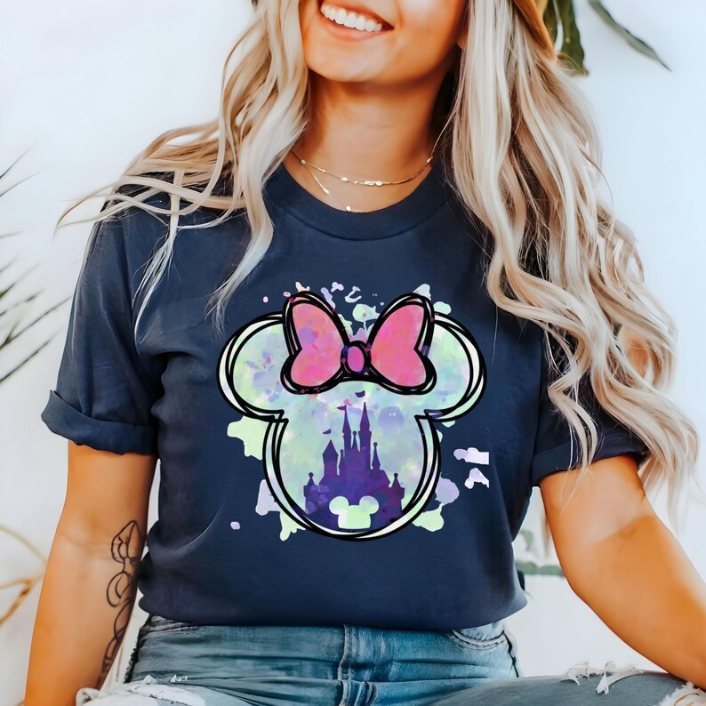 May include: A navy blue t-shirt with a watercolor-style graphic of Mickey Mouse's head with a pink bow and a silhouette of Cinderella's castle inside.