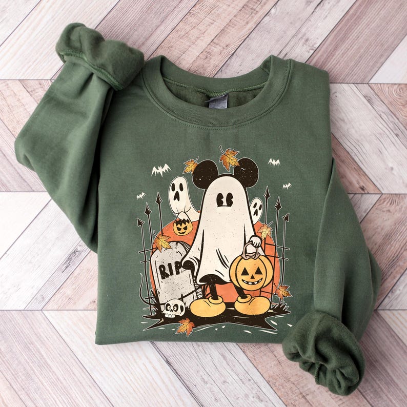 May include: Green sweatshirt with a vintage-style illustration of a ghost Mickey Mouse holding a jack-o'-lantern. The ghost is surrounded by bats, a tombstone that says "RIP", and other Halloween imagery.