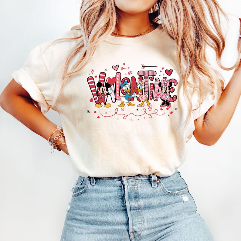 K&ouml;nnte beinhalten: Ein wei&szlig;es T-Shirt mit einem pinkfarbenen und roten Grafikdesign mit Mickey Mouse, Minnie Mouse und Donald Duck. Die Grafik sagt "Valentine" mit Herzen und Pfeilen.