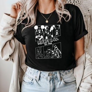 K&ouml;nnte beinhalten: Schwarzes T-Shirt mit einem wei&szlig;en Aufdruck von Mickey Mouse, Minnie Mouse, Donald Duck und Goofy. Der Aufdruck enth&auml;lt den Text "Mickey & Co. Est. 1928".