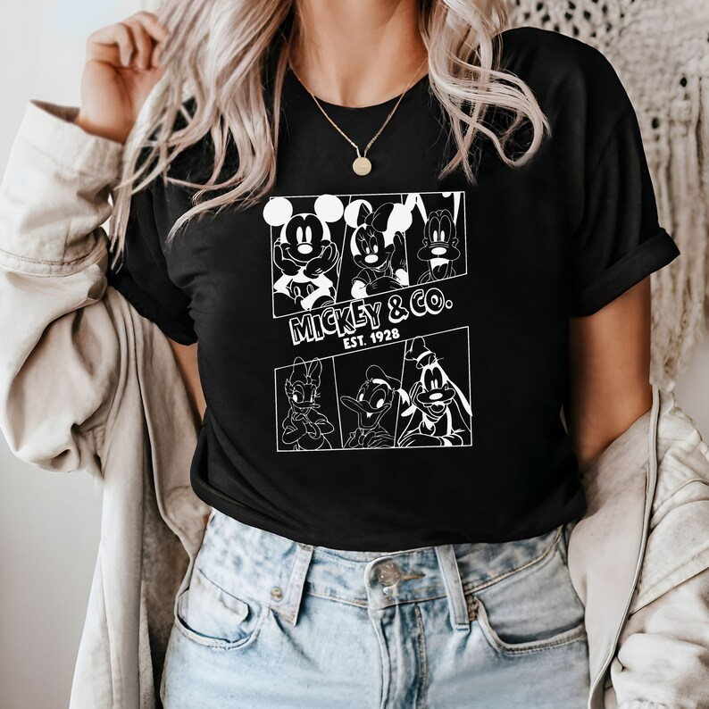 K&ouml;nnte beinhalten: Schwarzes T-Shirt mit einem wei&szlig;en Aufdruck von Mickey Mouse, Minnie Mouse, Donald Duck und Goofy. Der Aufdruck enth&auml;lt den Text "Mickey & Co. Est. 1928".