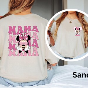 Puede incluir: Camiseta color arena con un dise&ntilde;o de Minnie Mouse y la palabra "MAMA" en rosa repetida varias veces. La parte delantera tiene un dise&ntilde;o m&aacute;s peque&ntilde;o de Minnie Mouse con la palabra "MAMA".
