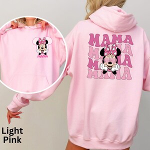 Puede incluir: Sudadera con capucha rosa claro con un dise&ntilde;o de Minnie Mouse en la parte delantera y trasera. La parte delantera muestra la cara de Minnie y la palabra "Mama". La parte trasera repite "Mama" con la cara de Minnie en el centro. La sudadera tiene un bolsillo delantero.
