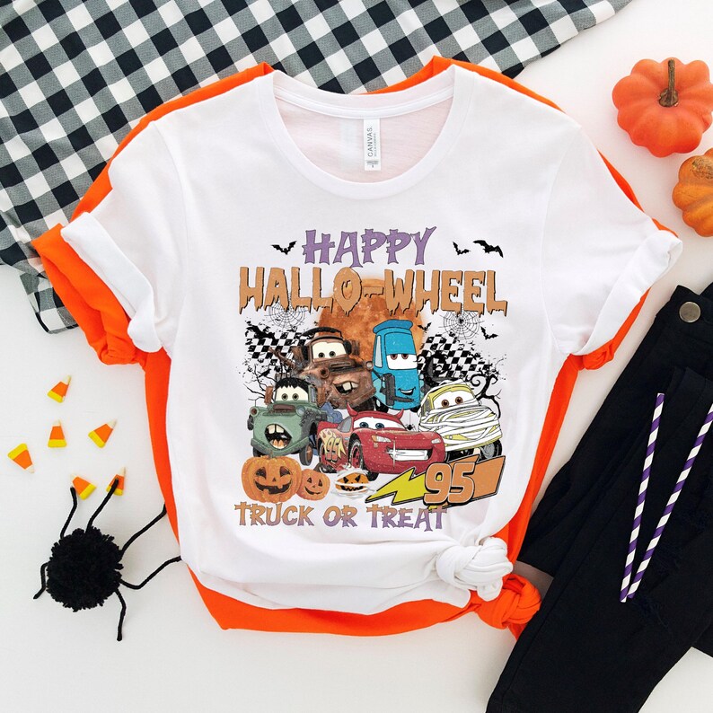 May include: White t-shirt with a graphic of cartoon cars dressed up for Halloween. The text reads "Happy Hallo-Wheel Truck or Treat".