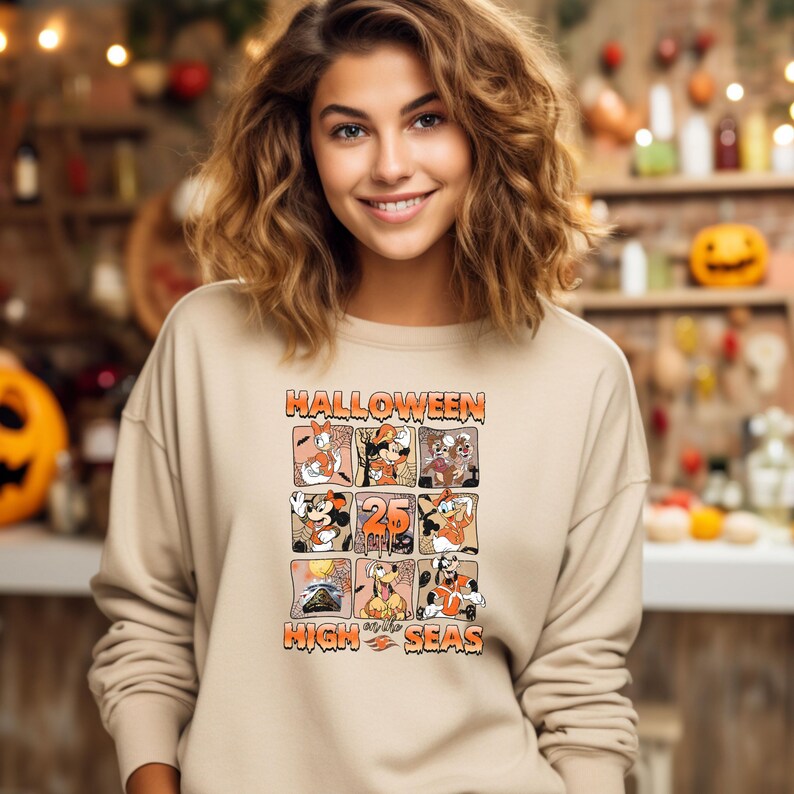 May include: A tan sweatshirt with a graphic print of Mickey Mouse and friends celebrating Halloween on the high seas. The text "Halloween High Seas" is printed on the sweatshirt.