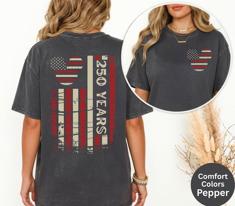 May include: Pepper-colored t-shirt featuring a distressed American flag design with a Mickey Mouse head and the text "250 YEARS" in red and white. The shirt has a crew neck and short sleeves. The shirt is part of the Comfort Colors collection.