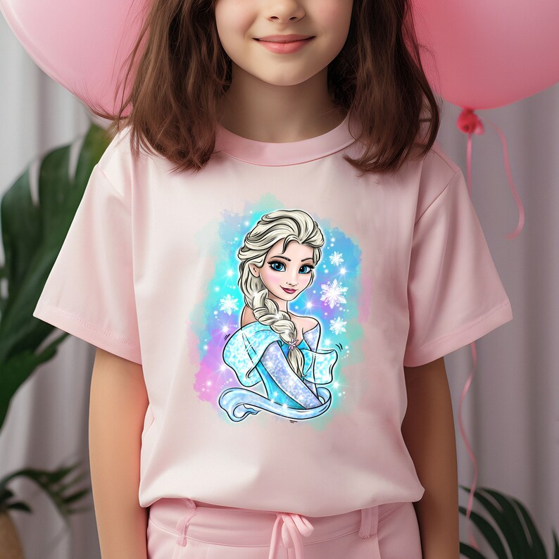 Op de afbeelding: Een roze T-shirt met korte mouwen met een kleurrijke illustratie van Elsa uit Frozen. De illustratie toont Elsa met haar kenmerkende vlecht en een blauwe en witte jurk. De achtergrond is een aquarelontwerp met sneeuwvlokken.