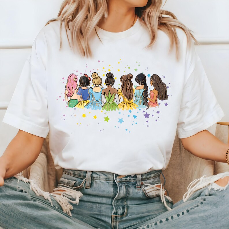 May include: White t-shirt with a colorful illustration of seven princesses standing back to back with stars in the background.