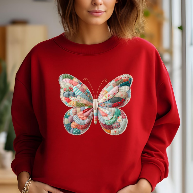 May include: A red sweatshirt featuring a large, colorful butterfly design. The butterfly is made of patchwork fabric in various colors and patterns, including red, blue, green, and white. The sweatshirt has a crew neck and long sleeves.