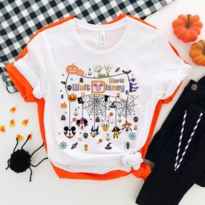 May include: White t-shirt with a Halloween-themed design featuring Mickey Mouse, Minnie Mouse, Donald Duck, Goofy, and Pluto. The design includes a spiderweb, pumpkins, and the text "Walt Disney World".