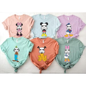 May include: Six pastel-colored t-shirts featuring cartoon characters with Stormtrooper helmets. Characters include Minnie Mouse, Mickey Mouse, Donald Duck, Goofy, Pluto, and Daisy Duck. The shirts are in shades of pink, blue, lavender, green, and orange.