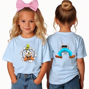 K&ouml;nnte beinhalten: Hellblaue T-Shirts mit einem Cartoon-Design von Goofy. Ein Shirt zeigt Goofy, der aus einem zerrissenen Loch herauskommt, das andere zeigt seine Beine. Die Shirts werden mit blauen Jeans kombiniert.