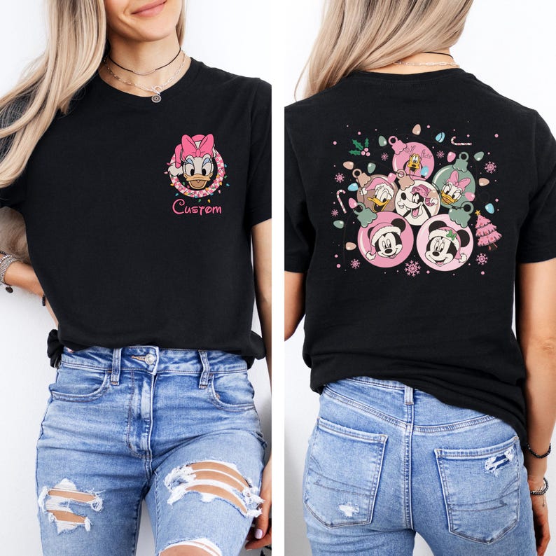 May include: Black t-shirt featuring a Daisy Duck graphic with the word "Custom" in pink. The back of the shirt displays a festive design with Mickey and Minnie Mouse, Donald and Daisy Duck, and other characters in Christmas ornaments.