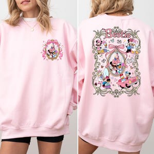 May include: Pink sweatshirt with a graphic of Mickey Mouse and friends in a vintage-inspired design. The text "Bestie" is printed on the back of the sweatshirt.