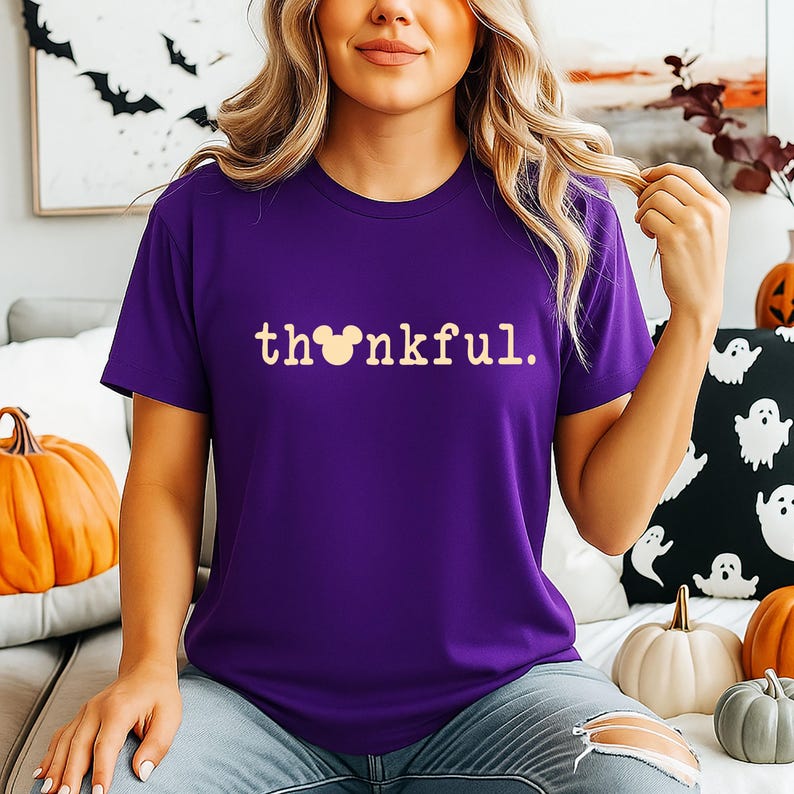 Puede incluir: Una camiseta morada con la palabra "thankful" en una fuente beige claro. La "o" de la palabra se reemplaza con una cabeza de Mickey Mouse. La camiseta es parte de una colecci&oacute;n tem&aacute;tica de Halloween.