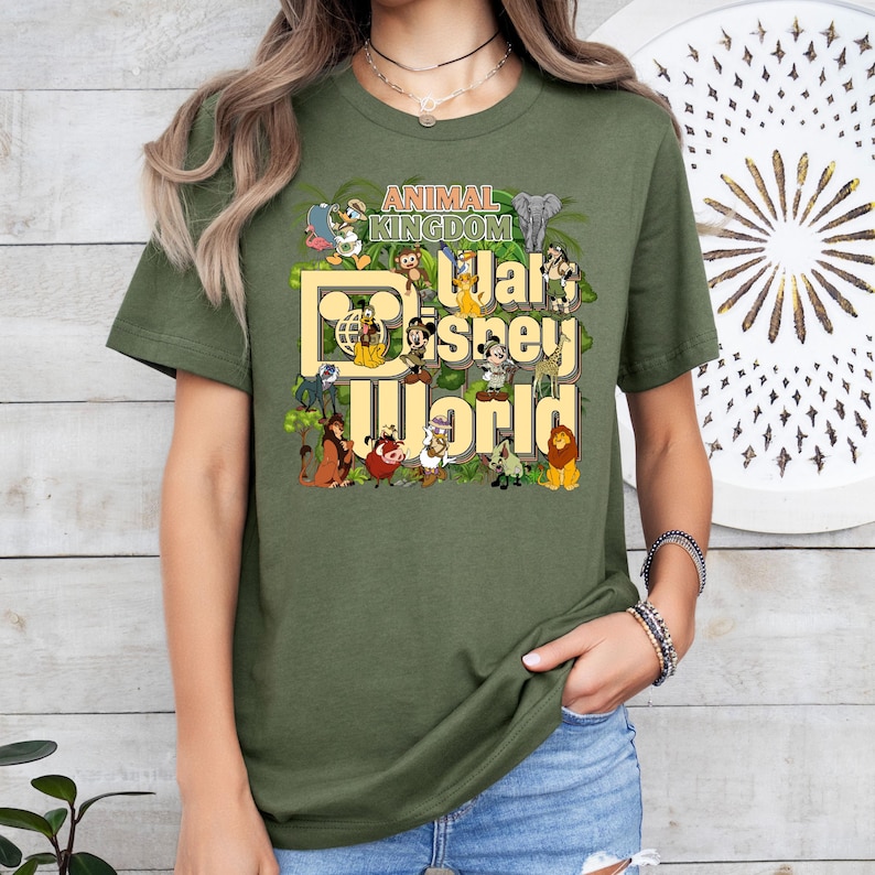 Pu&ograve; includere: Una maglietta verde con una stampa grafica di vari personaggi Disney e il testo "Animal Kingdom Walt Disney World".