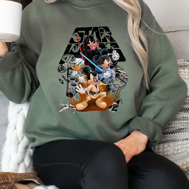May include: A green sweatshirt with a graphic print of Mickey Mouse, Donald Duck, Goofy, and Minnie Mouse dressed as Star Wars characters. The text "Star Wars" is printed above the characters.