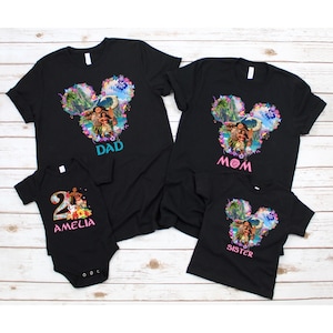 May include: Black family matching t-shirts and a onesie. The shirts feature a colorful graphic in the shape of Mickey Mouse ears with a tropical scene and the words "Dad", "Mom", and "Sister". The onesie says "Amelia" and "2".
