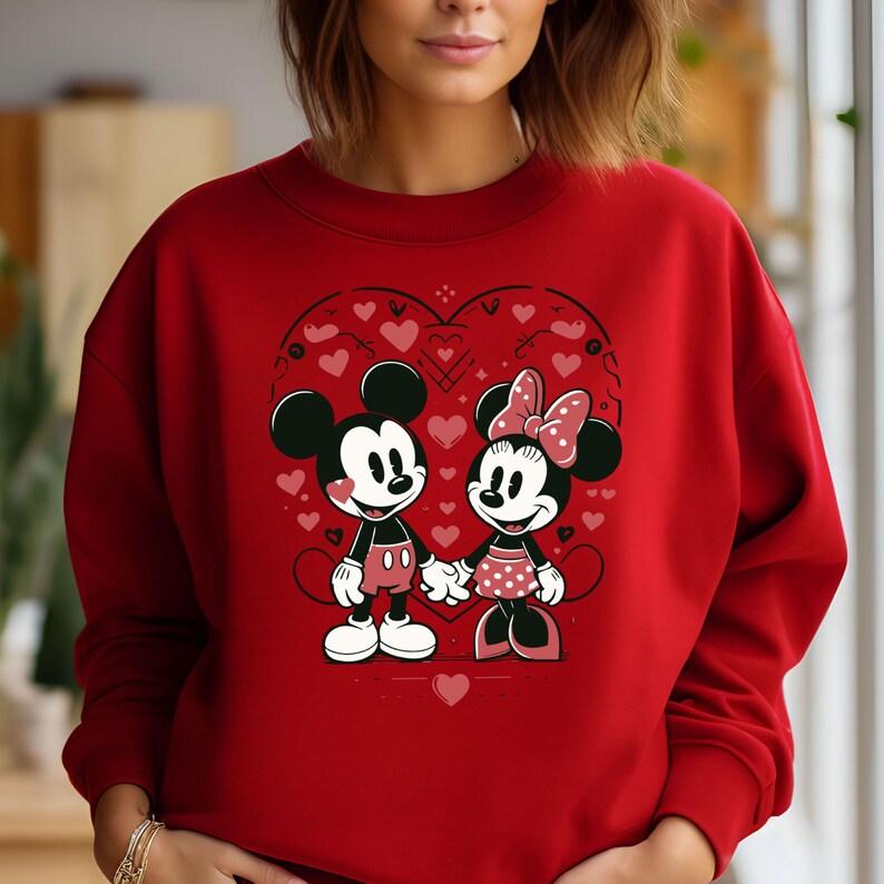 May include: Red sweatshirt with a graphic of Mickey Mouse and Minnie Mouse holding hands inside a heart shape with hearts and other designs around them.