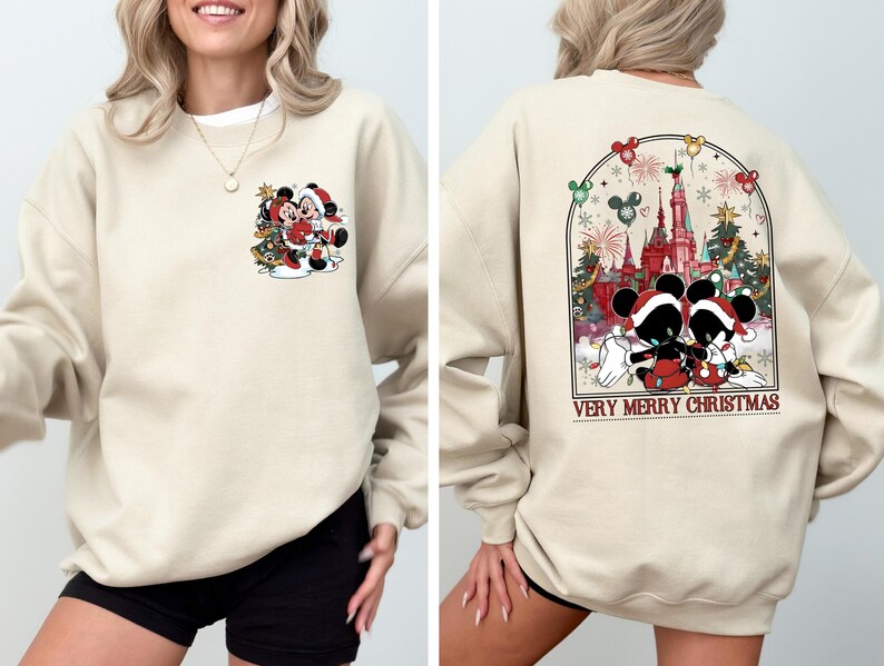 May include: A beige sweatshirt with a Christmas-themed design featuring Mickey Mouse and Minnie Mouse. The front of the sweatshirt has a small image of Mickey and Minnie standing in front of a Christmas tree. The back of the sweatshirt has a larger image of Mickey and Minnie standing in front of Cinderella's Castle at Disney World. The text "Very Merry Christmas" is printed below the image.